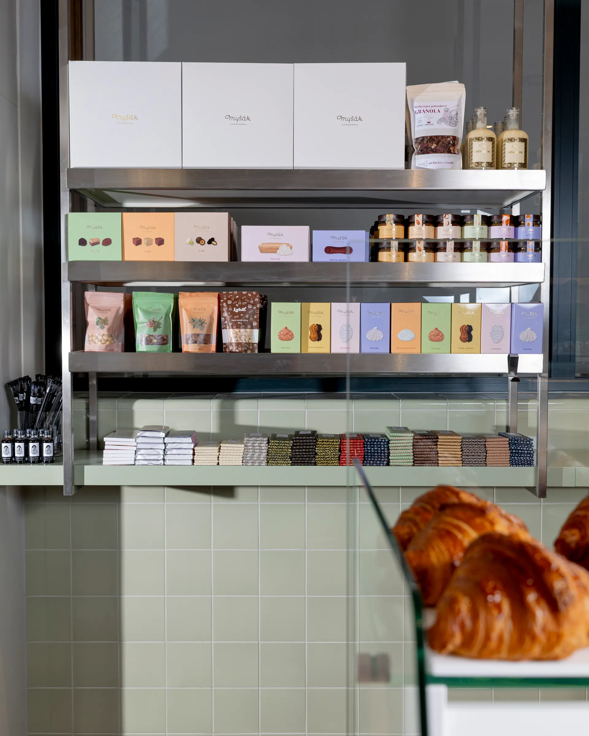 Regál s balenými produkty Myšák a čerstvými croissanty v cukrárně.